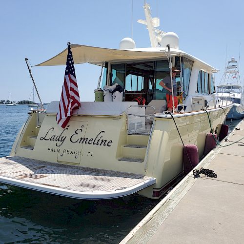 A docked yacht named "Lady Emeline" with people on board, American flag at the back, and clear skies in the background.