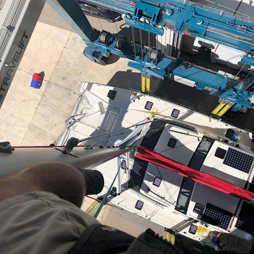 The image shows a view looking down from a height, focusing on industrial equipment, possibly on a crane, and a person&rsquo;s knee in the bottom left corner.