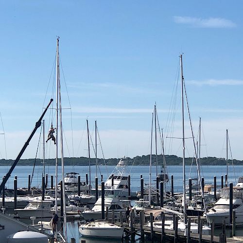 The image shows a marina with numerous sailboats and yachts docked, calm blue waters, and a clear sky with minimal clouds in the background.